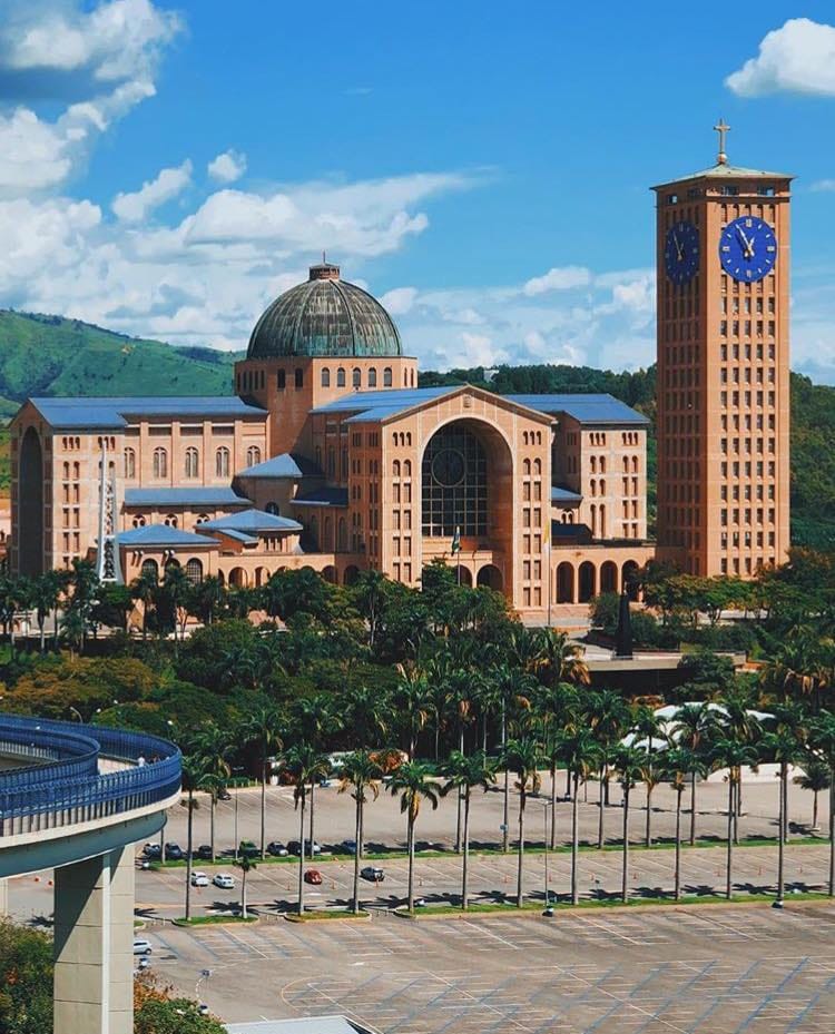 Vista externa da Basílica de Nossa Senhora Aparecida sob céu azul, destacando a arquitetura imponente do maior santuário mariano do mundo.