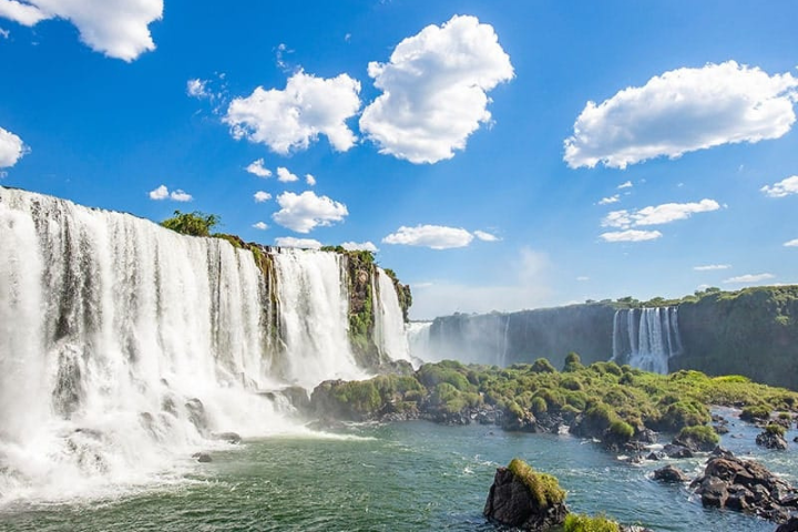 Vista panorâmica das quedas d'água das Cataratas do Iguaçu com arco-íris e vegetação exuberante ao redor.