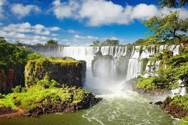 Vista panorâmica das quedas d'água das Cataratas do Iguaçu com arco-íris e vegetação exuberante ao redor.