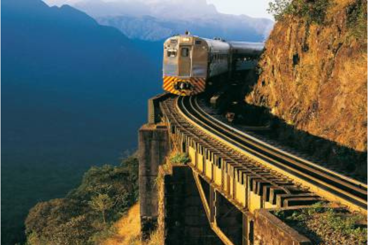 Trem turístico de passageiros atravessando ponte histórica na Serra do Mar paranaense, rodeado por mata atlântica densa.